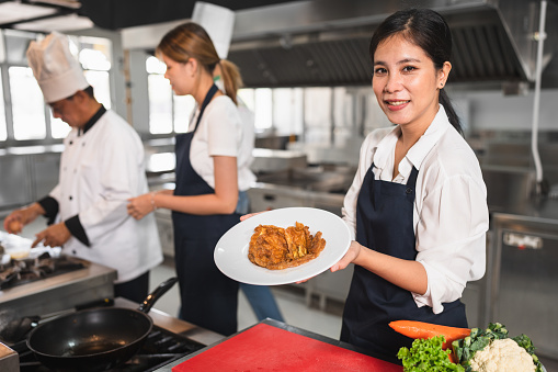 Happy student Asia woman assistant chef holding omelet with kitchen background