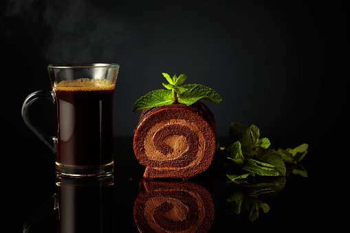 Chocolate cake with mint and a mug of black coffee on a black reflective background. Copy space.