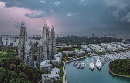 The Keppel Bay area in Singapore is a modern, luxury residential district full of skyscrapers, big yachts in the marina and tropical rainforest. In the background a dramatic sky and thunder lightning.