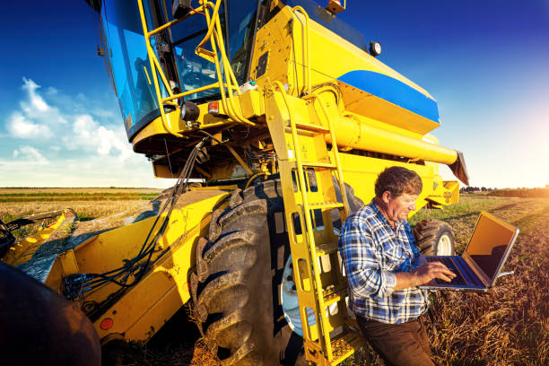 istock A farmer leaning against a combine harvester uses a computer during harvest. 1468743146