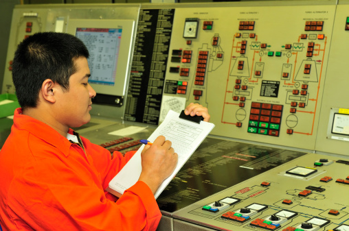 A shipping engineer near a panel of ship's automation filling a log records