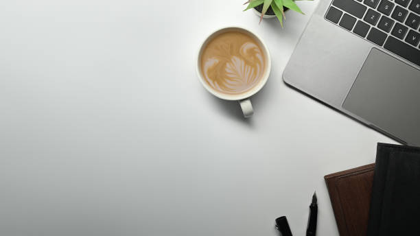 istock Top view of laptop computer, coffee cup, potted plant and notebook on white working desk. Top view with copy space. 1468756438