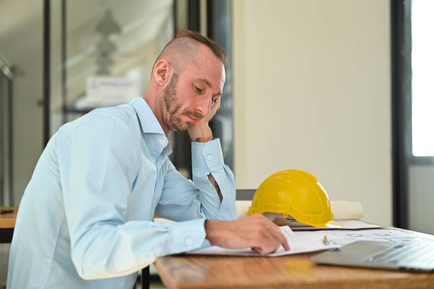 istock Serious adult caucasian engineer man checking plan and working with blueprint at his office desk. 1468756525