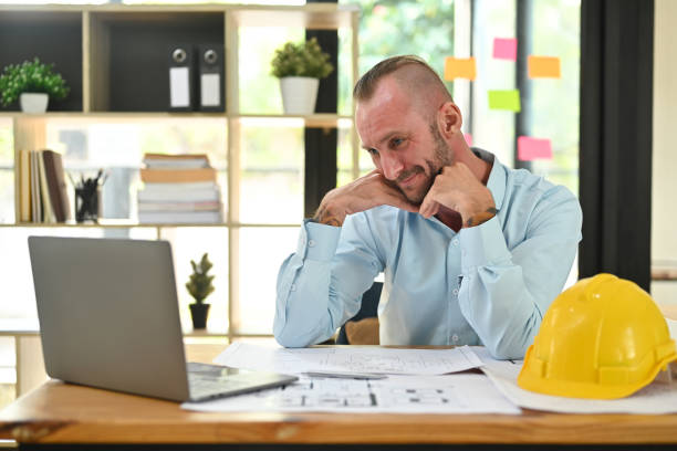 istock Smiling engineers man looking at laptop screen while working with blueprints at office. Engineer, construction concept. 1468756723