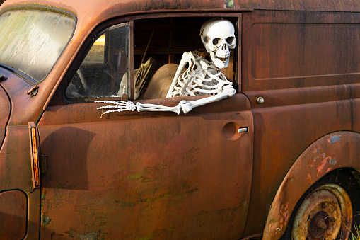 Human skeleton sitting in a rusty old car and looking out of the window