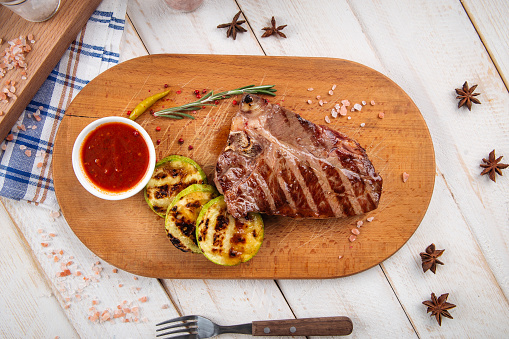 Grilled beef steak with squash slices and red sauce on the wooden board