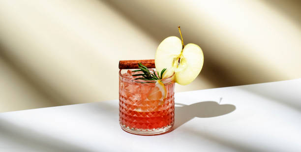 coquetel alcoólico de torta de maçã com vodka, licor de maçã, canela, limão, decorado com alecrim. fundo bege claro, luz dura, padrão de sombra, banner - red apple fotos - fotografias e filmes do acervo