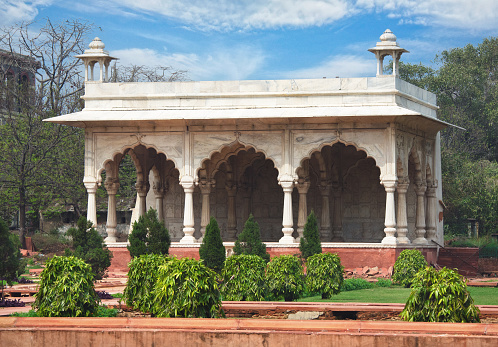The photo captures the stunning Bhadon Pavilion, one of two identical structures located on opposite ends of the canal within the magnificent Red Fort in Delhi, India. The Sawan and Bhadon Pavilions are named after the two rainy months in the Hindu calendar during the monsoon. It served as a resting place for the shah and his court. The pavilion features a white marble facade adorned with intricate carvings and delicate patterns, showcasing the exceptional craftsmanship of the Mughal era.  Its timeless elegance make it a must-visit attraction for anyone exploring the Red Fort. The photo aptly captures the grandeur of the Bhadon Pavilion, with its intricate detailing and white marble facade standing out against the clear blue sky.