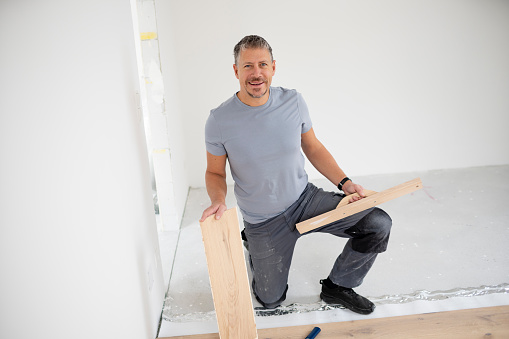 Middle aged man with grey hair and grey shirt laying parquet floor in new loft, house