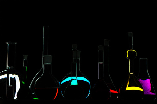 Flasks containing various colored liquids on dark background.