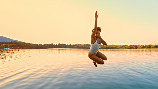 Young woman jumping in lake during sunset.