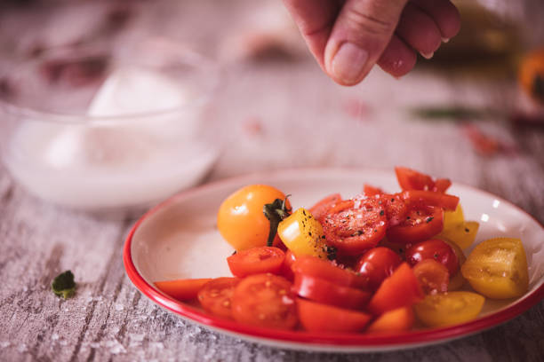 Sprinkling salt on Tomatoeas with mozzarella in a bowl in the background