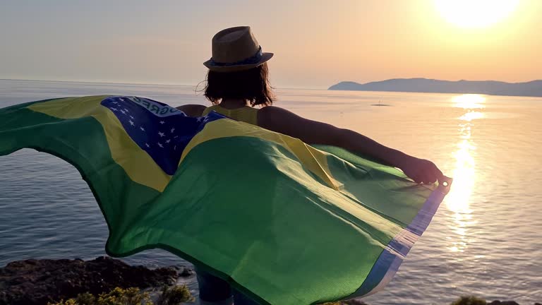 Young Caucasian woman waving a Brazilian flag on the seaside during sunset