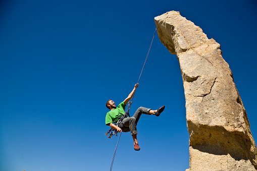 A rock climber rappelling from a rock spire in Joshua Tree National Park, California on a summer day.