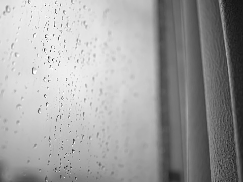 Closeup of rain drops on the window glass with curtain in the room. Black and white abstract background