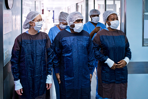 Multiracial team of female and male surgeon wearing surgical caps and masks standing in medical clinic.