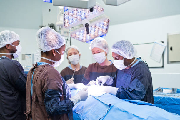 equipo de cirujanos que operan al paciente iluminado en la sala de emergencias del hospital - hair net nurse scrubs asian ethnicity fotografías e imágenes de stock