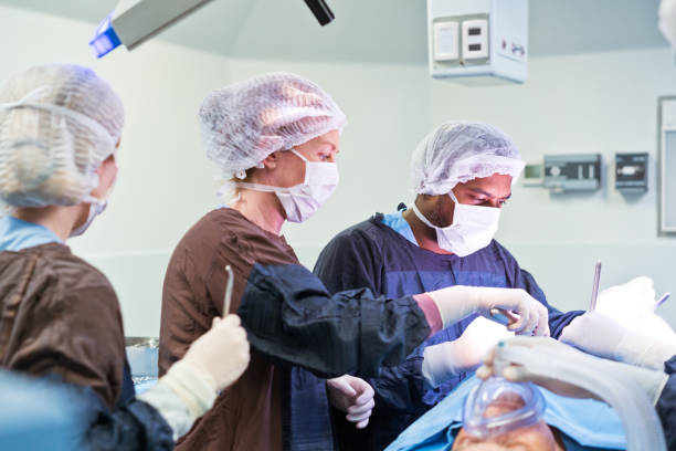 equipo de cirujanos que operan al paciente iluminado en la sala de emergencias del hospital - hair net nurse scrubs asian ethnicity fotografías e imágenes de stock