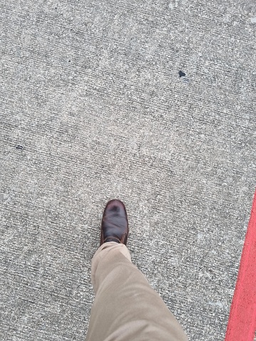 Man standing at the border line on urban pavement, top view of young male feet wearing sneakers, waiting behind the line, immigration concept