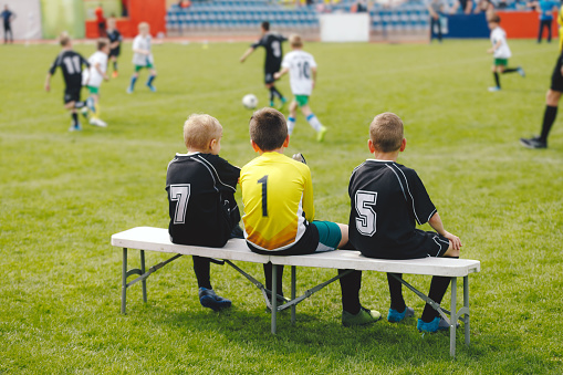 Young boys in soccer jerseys sitting on the substitute players' bench. Children play sports during school tournaments. Kids having fun attending sports competition
