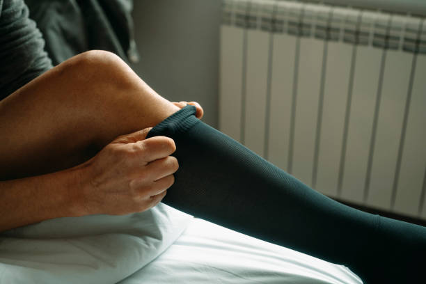 man putting on a compression sock sitting on the bed stock photo