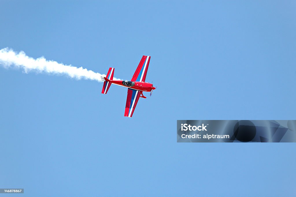 aerial acrobatics stunt flying aerial acrobatics - red propeller plane with smoke trail against clear blue sky Aerobatics Stock Photo