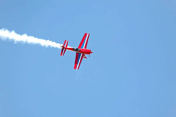 aerial acrobatics - red propeller plane with smoke trail against clear blue sky