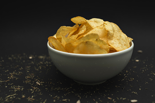 White ceramic bowl with golden potato chips on a black background.