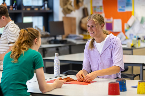 Group of students participating in an art class while at school in the North East of England. They are using modelling clay, laughing together.