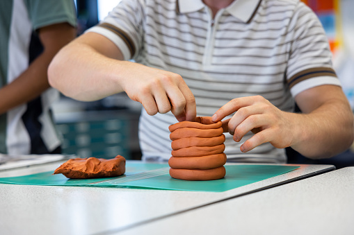 Close up of a male student participating in an art class while at school in the North East of England. He using modelling clay.
