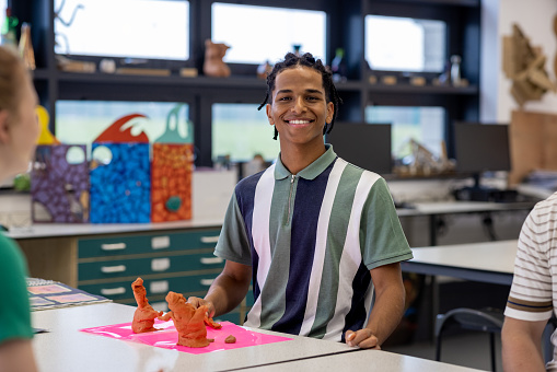 Medium shot of a male student participating in an art class while at school in the North East of England. He using modelling clay, smiling while looking at the camera.