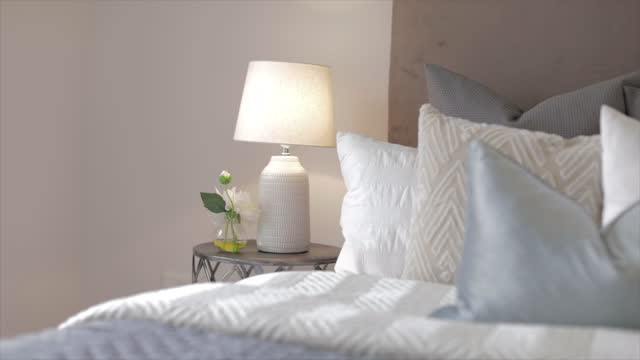 Soft light from a bedside lamp illuminating a vase with beautiful flowers beside a comfortable bed with a soft knitted blanket to snuggle into on a cold winter day.