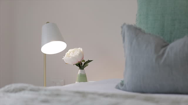 Soft light from a bedside lamp illuminating a single rose beside a comfortable bed with a soft knitted blanket to snuggle into on a cold winter day.