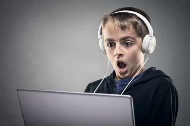 Shocked and surprised teenag boy on the internet with laptop computer concept for amazement, astonishment, making a mistake, stunned and speechless or seeing something he shouldn't see