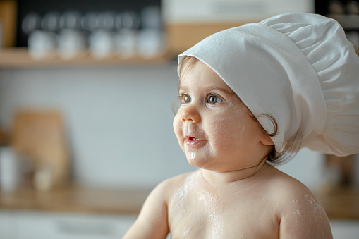 Portrait image of baby boy wearing a chef's hat with kitchen background