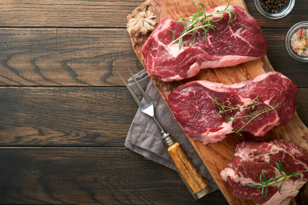 raw beef steak. marbled raw fresh ribeye steak with rosemary, salt and pepper on cutting board on dark concrete background. raw beef steak and spices for cooking. - flatware silverware in a row eating utensil imagens e fotografias de stock