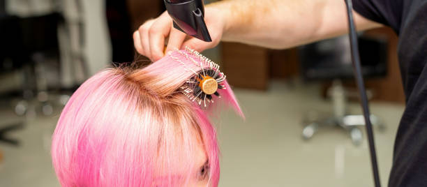 미용실에서 남성 미용사의 손에 의해 검은 헤어 드라이어와 검은 둥근 브러시로 젊은 백인 여성의 짧은 분홍색 머리를 말리고 닫습니다. - frizzy human hair hairdresser hair dryer 뉴스 사진 이미지
