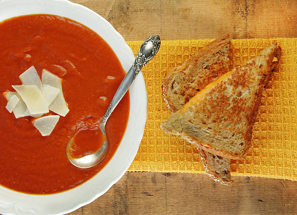 Grilled cheese sandwich and bowl of homemade tomato soup on a rustic wooden table.