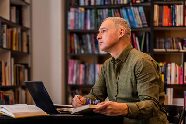 istock Mature man writing in book sitting by window 1468830854