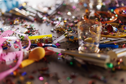 Close up shot of aftermath of a great celebratory party. Colorful confetti, half eaten cake slices empty glasses, cake fireworks, party horns, balloons and other decor.