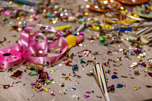Close up shot of aftermath of a great celebratory party. Colorful confetti, pink ribbon, party horns, balloons, cake fireworks.