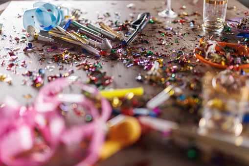 Close up shot of aftermath of a great celebratory party. Colorful confetti, half eaten cake slices empty glasses, cake fireworks, party horns, balloons and other decor.