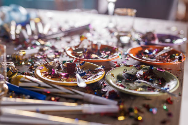 Close up shot of aftermath of a great celebratory party. Colorful confetti, half eaten cake slices empty glasses, cake fireworks, party horns, balloons and other decor.