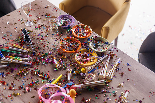 High angle view of aftermath of a great celebratory party. Colorful confetti, half eaten cake slices empty glasses, cake fireworks, party horns, balloons and other decor.