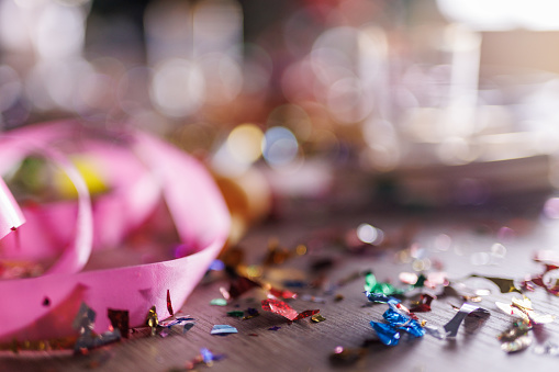 Close up shot of aftermath of a great celebratory party. Colorful confetti, half eaten cake slices empty glasses, cake fireworks, party horns, balloons and other decor.
