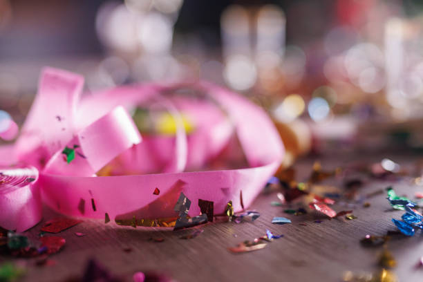 Close up shot of aftermath of a great celebratory party. Colorful confetti, half eaten cake slices empty glasses, cake fireworks, party horns, balloons and other decor.