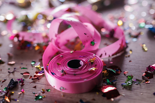 Close up shot of aftermath of a great celebratory party. Colorful confetti, pink ribbon and other decor.