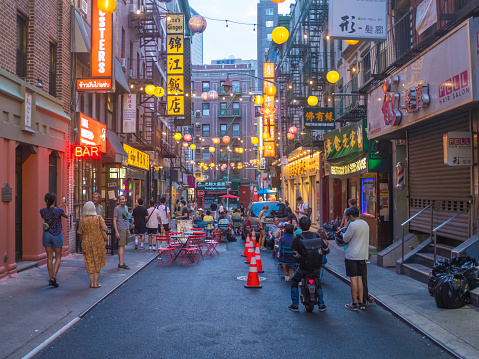 New York City, United States - August 21, 2022: A street of the Chinatown of New York City at dawn with lights and lanterns switched on and some people on the street