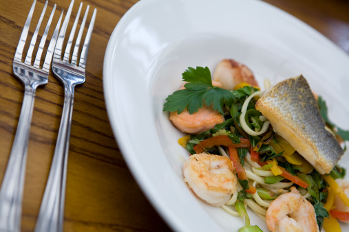 A slice of salmon on a bed of tiger prawns and fried vegetables.