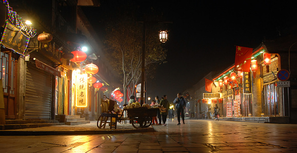 Pingyao in Shanxi Province, China: Street scene in Pingyao at night with city lights, red lanterns and Chinese flags. People walking in the old town.